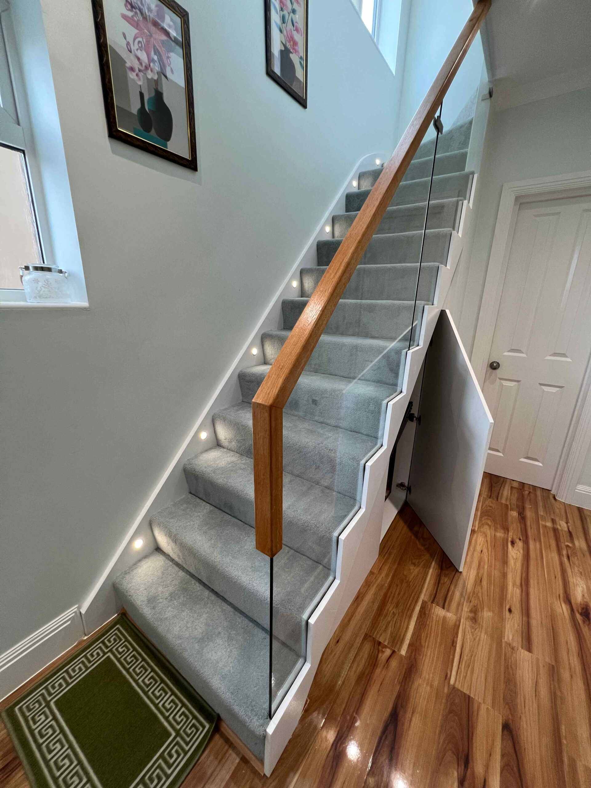 Grey carpeted staircase with glass balustrade and oak handrail on top