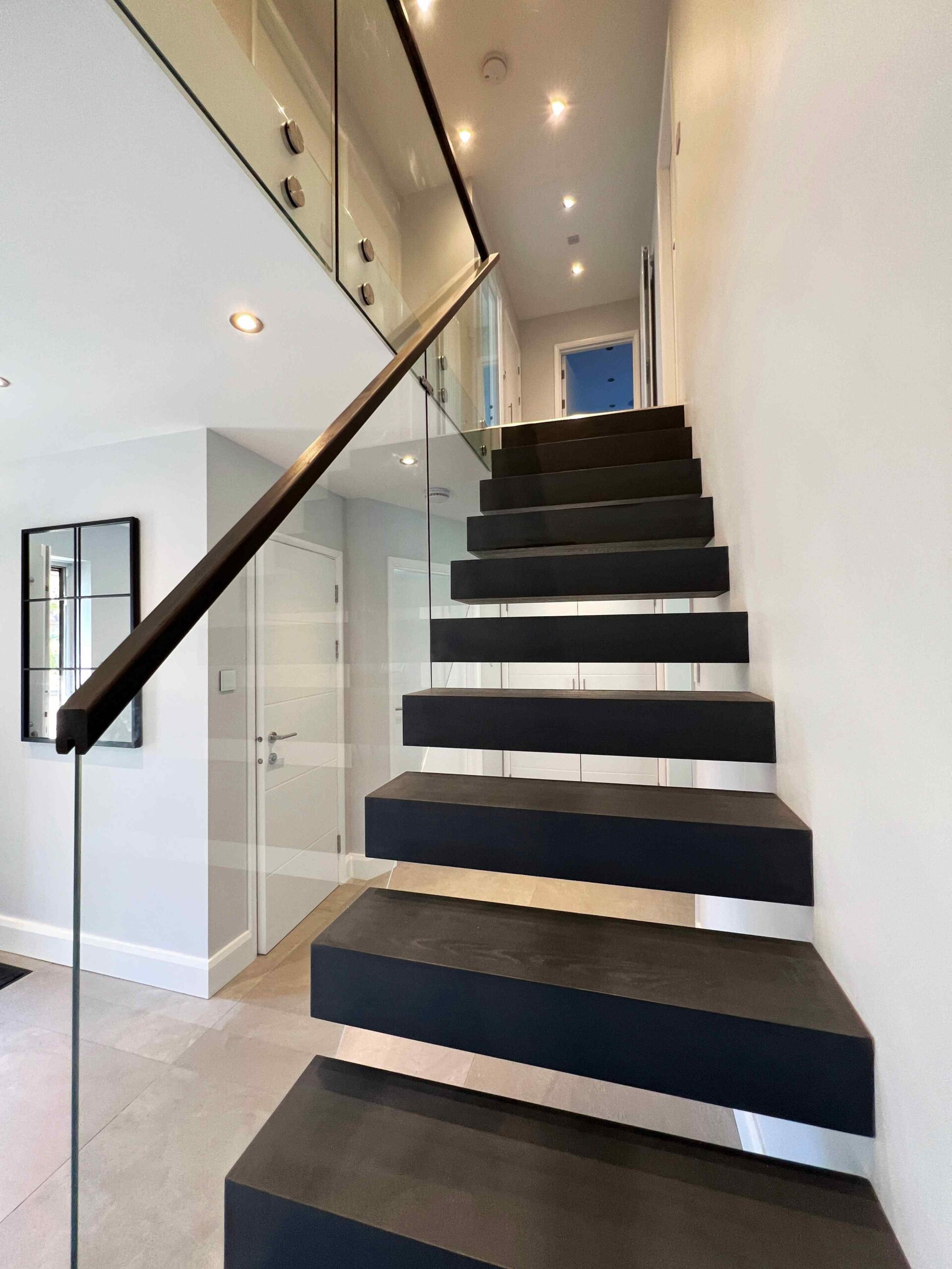 Floating staircase complemented with glass balustrade and black oak stair treads.