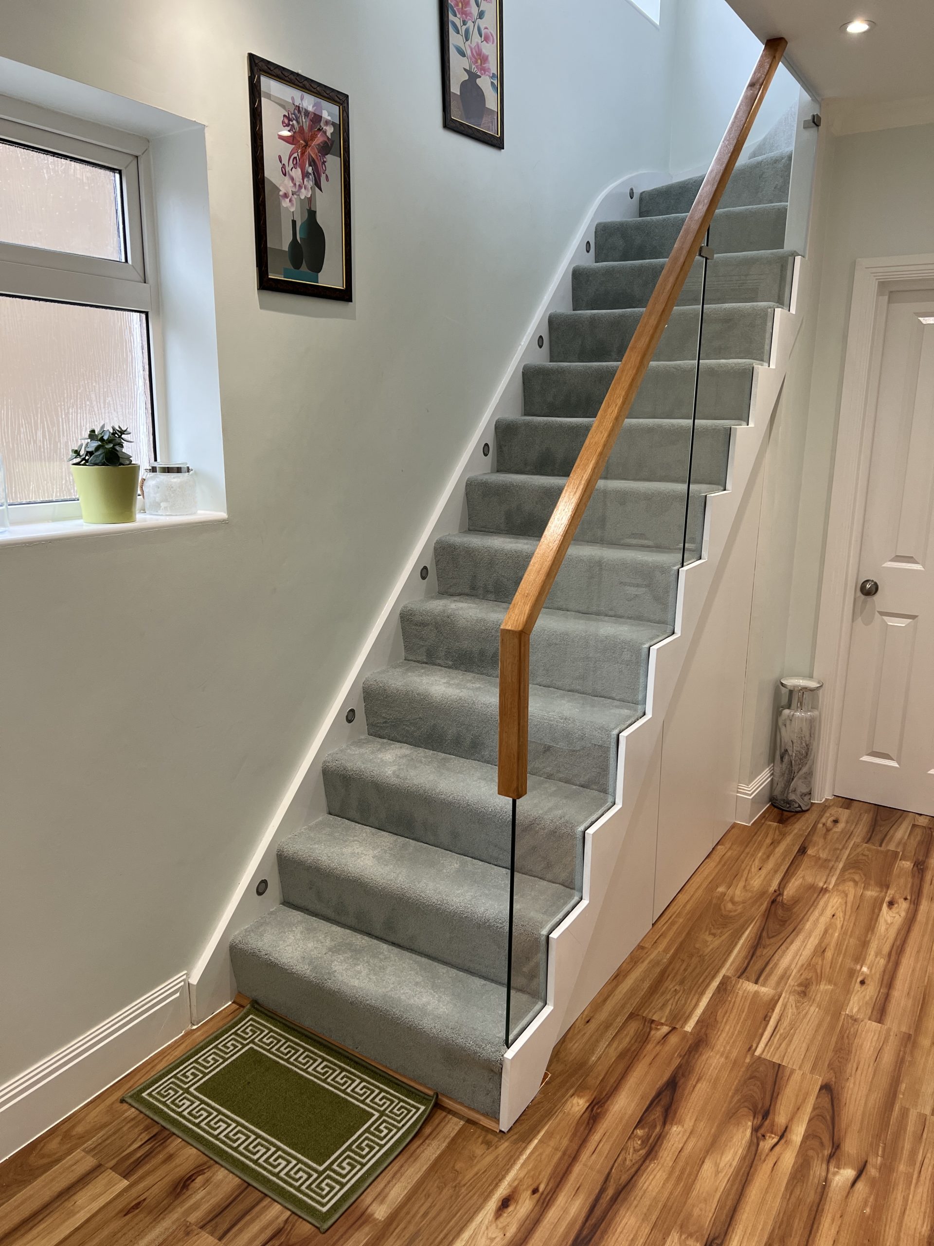 grey carpeted wooden staircase with glass balustrades